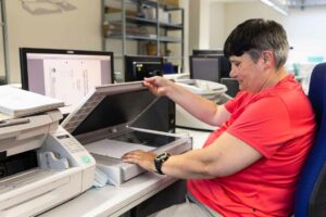 Eine Mitarbeiterin digitalisiert Unterlagen mit einem Flachbettscanner